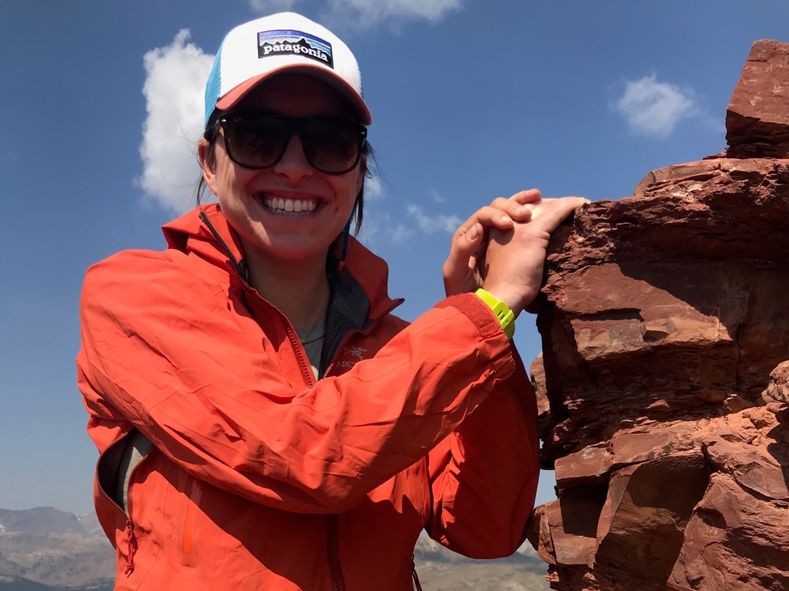 Nicole smiling beside red rock in the Colorado mountains.